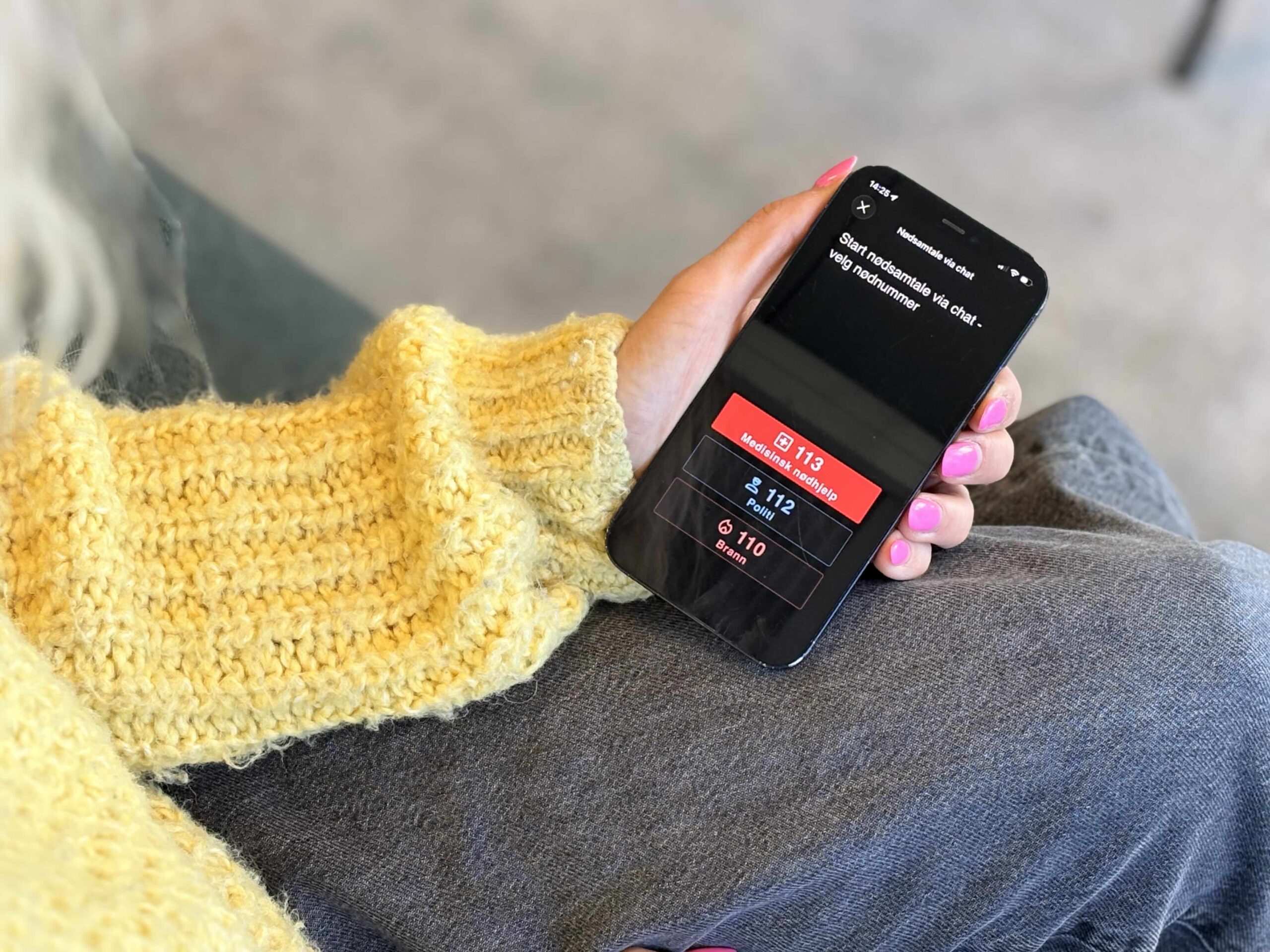 Bildet viser ei som holder en smarttelefon som viser chatløsning med nødnumrene 113, 112 og 110. 
